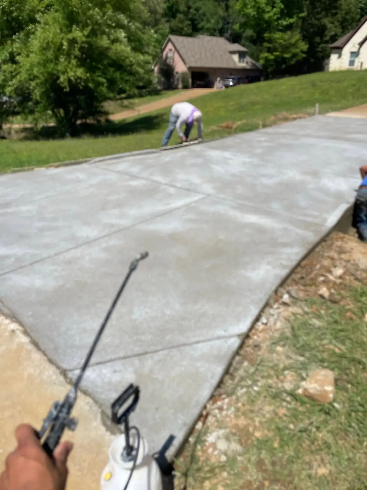 Worker finishing the far edge of a wide fresh concrete driveway