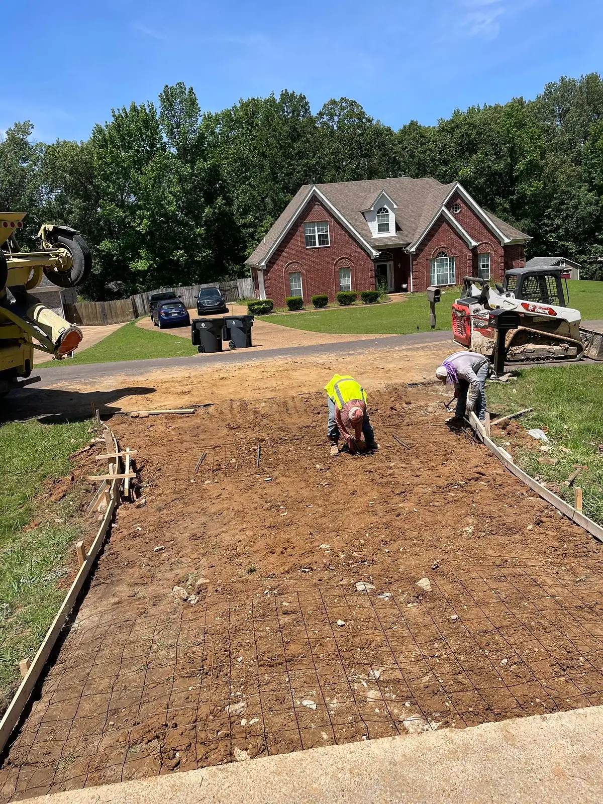 Crew laying reinforcing mesh across a driveway base before pouring