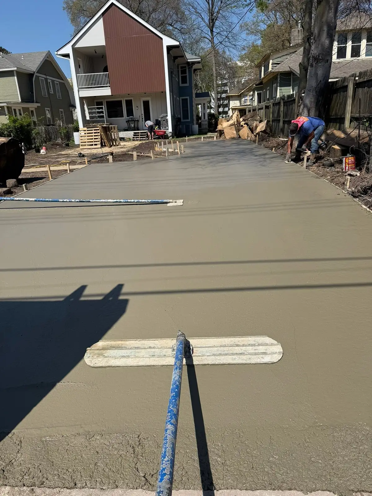 Fresh concrete slab being smoothed with a bull float under blue sky
