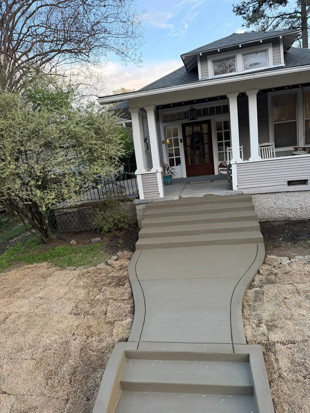 Sweeping concrete walkway and steps rising to a craftsman front porch