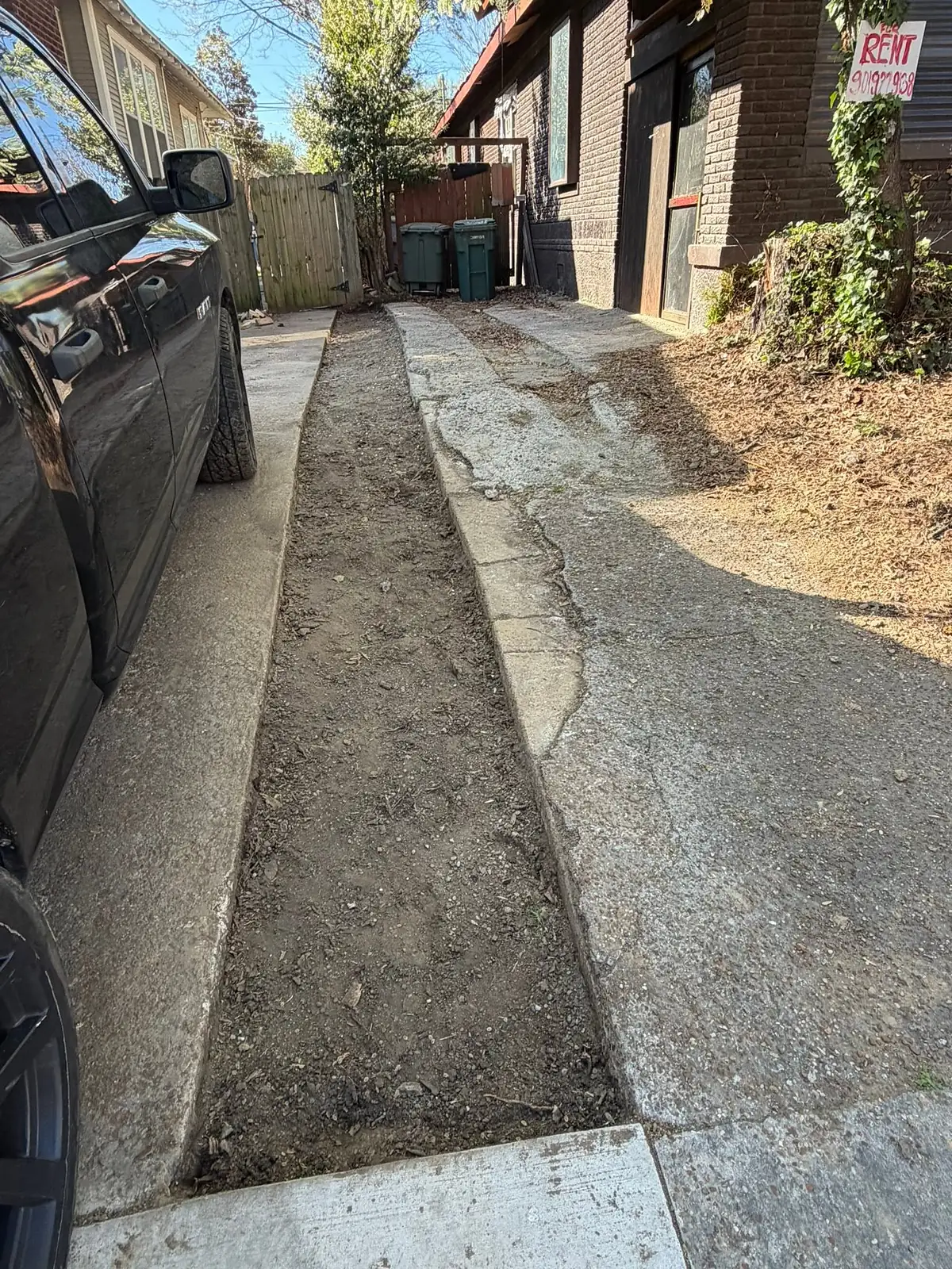Old cracked and sunken sidewalk beside a parked car before replacement