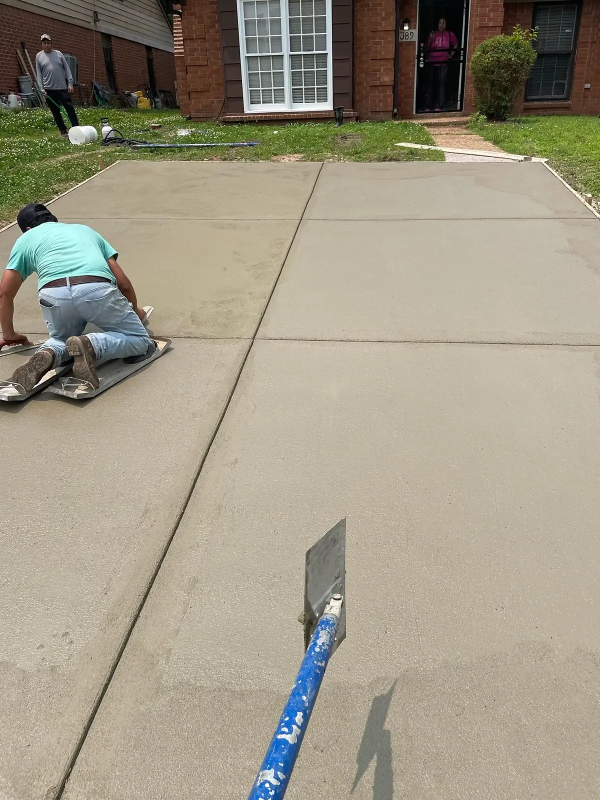Finisher on a kneeling board hand troweling a fresh concrete driveway