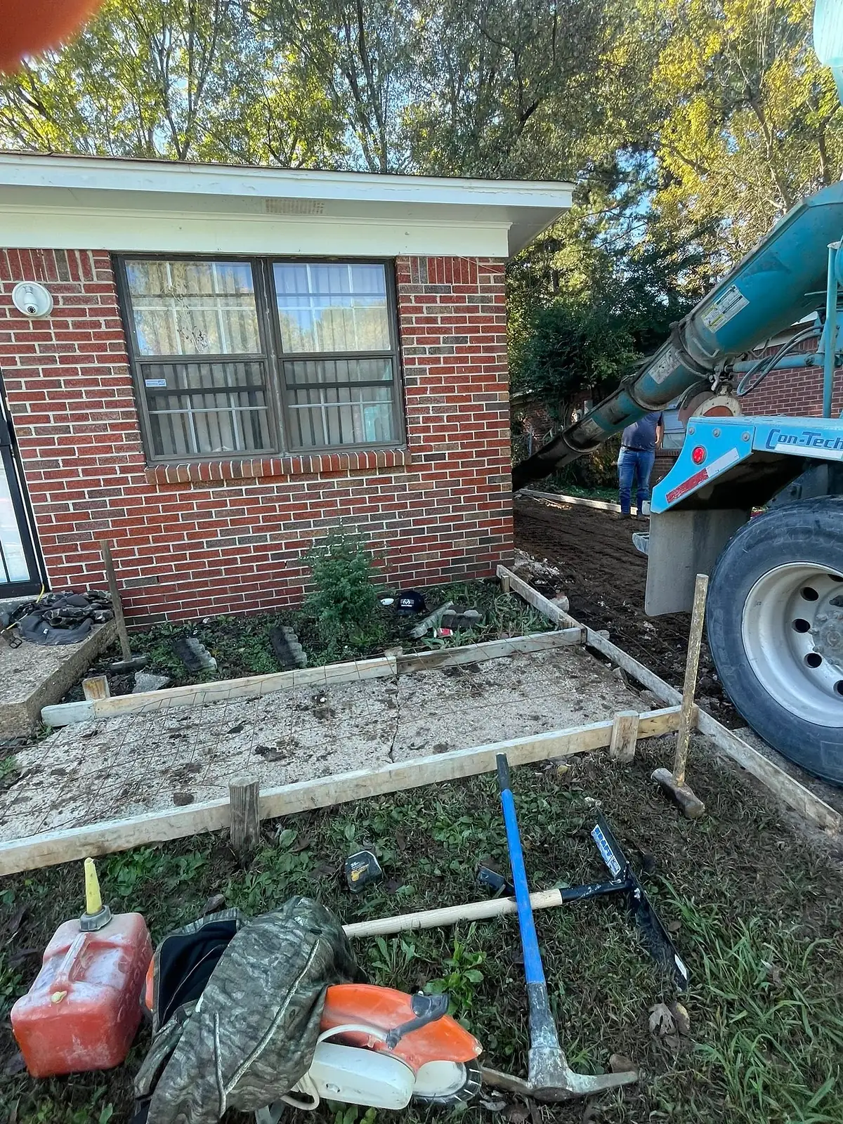 Small concrete pad formed and staked beside a brick wall