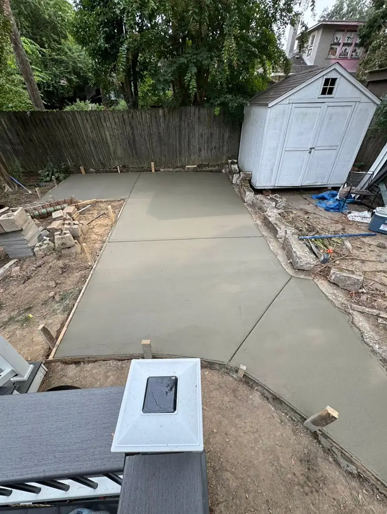Freshly poured backyard patio slab beside a white garden shed