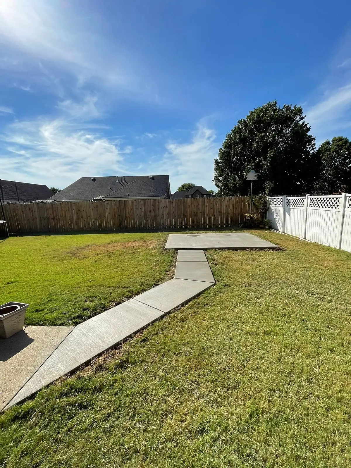 Concrete walkway crossing a green backyard toward a patio area