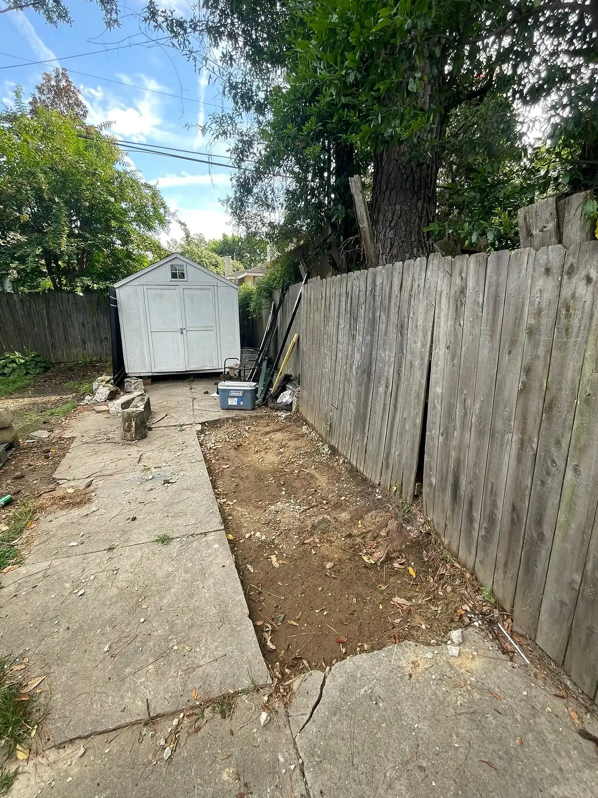 Side yard stripped back to bare soil beside a wooden fence before the pour