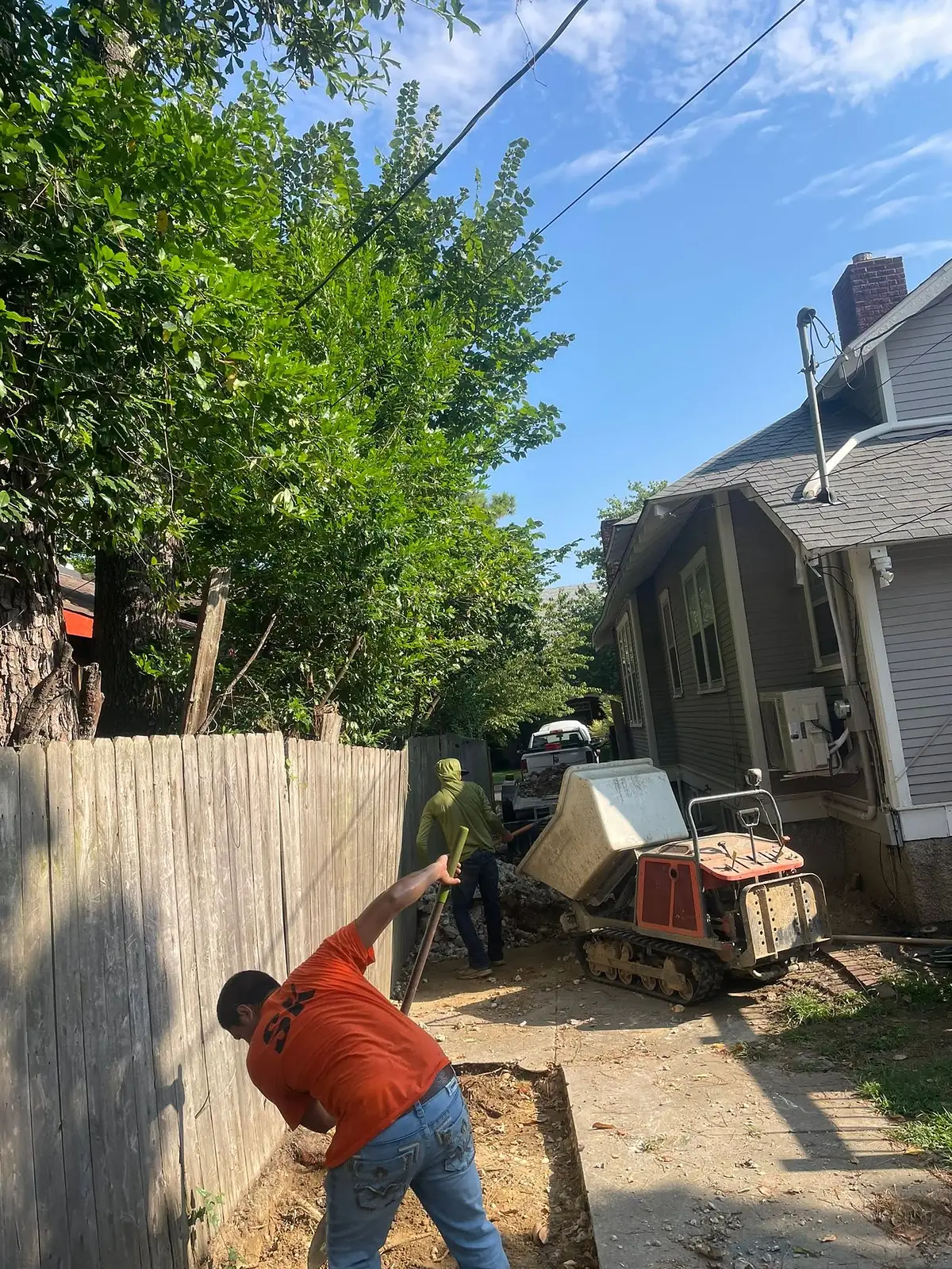 Worker digging out the old base along a fence line before pouring