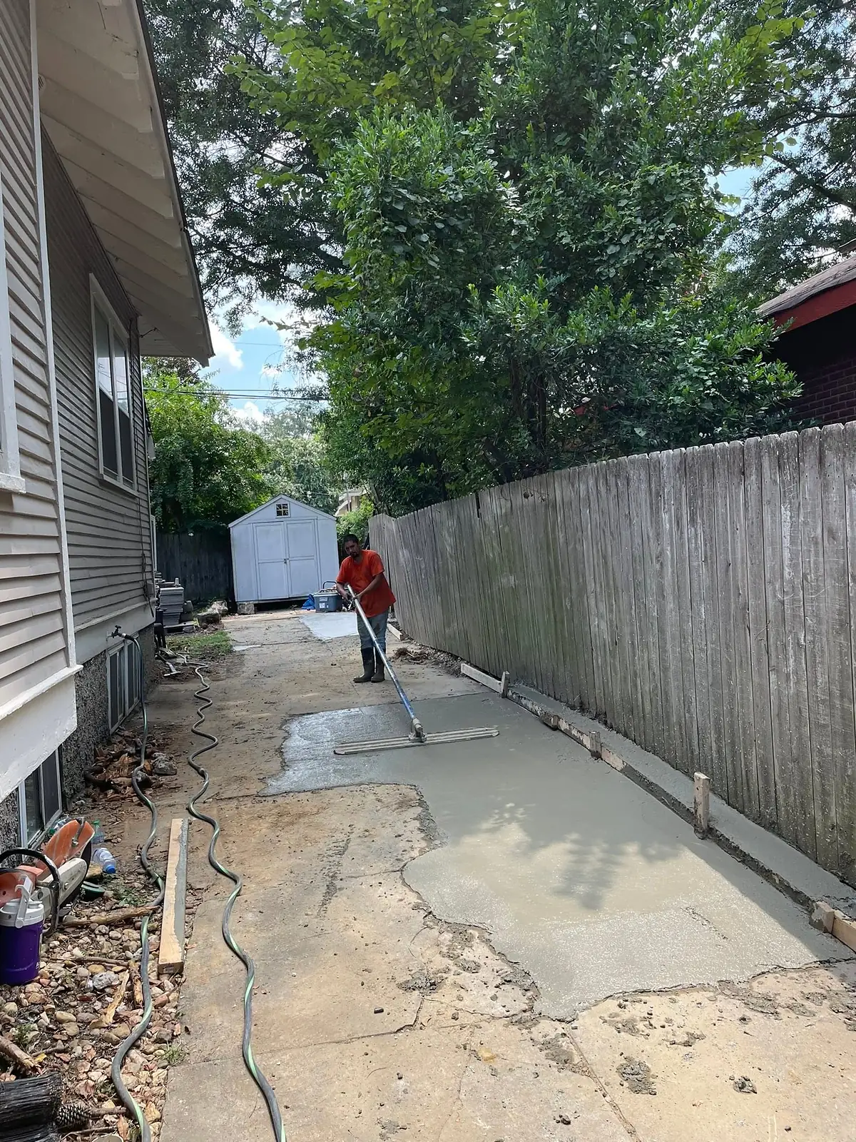 Worker raking fresh concrete into a narrow side yard form