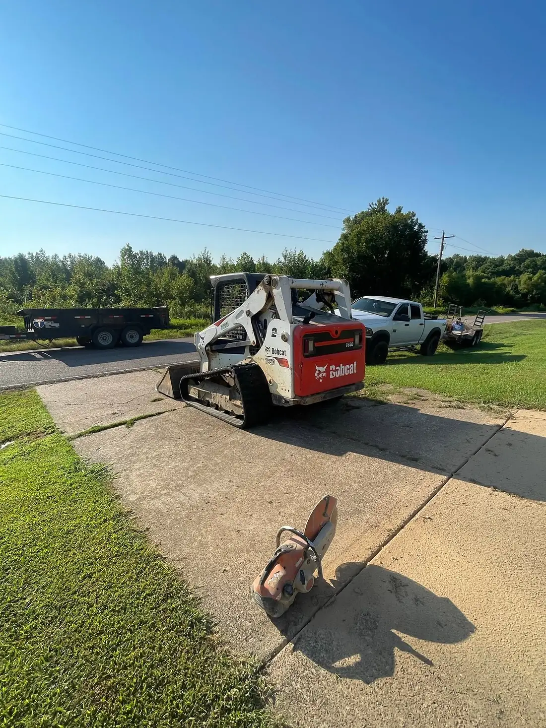 Skid steer and dump trailer on site during a driveway tear out