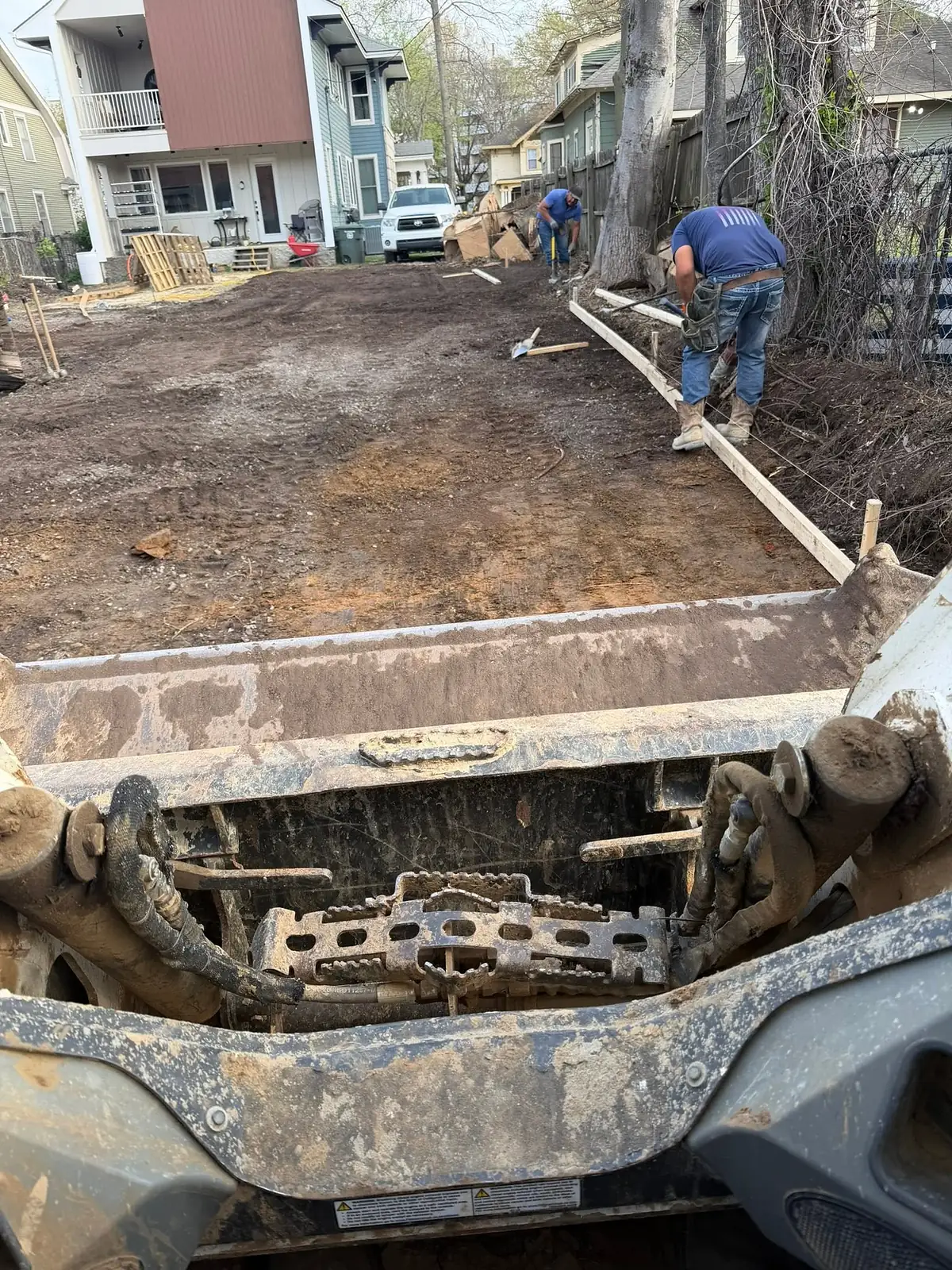 Worker setting timber forms next to a loaded dump trailer